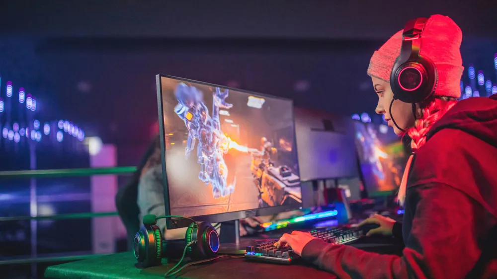 Alt Text: A woman gamer playing on a PC with LED lights set up with her Headset on 