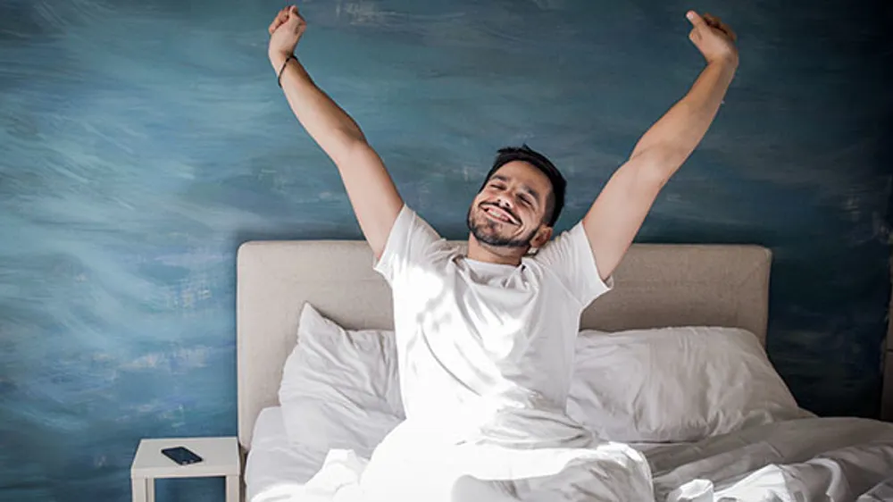ALT Text: a man in a white t-shirt stretching his arms like is just waking up